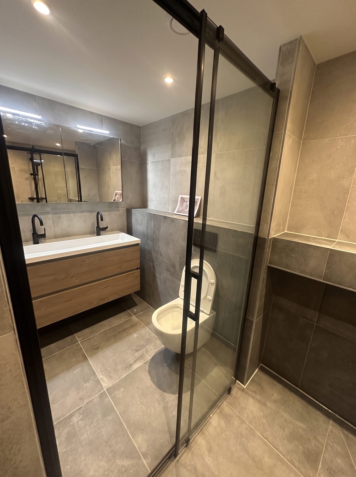 Badkamer met glazen schuifdeur-douche, houten wastafelmeubel en zwart sanitair