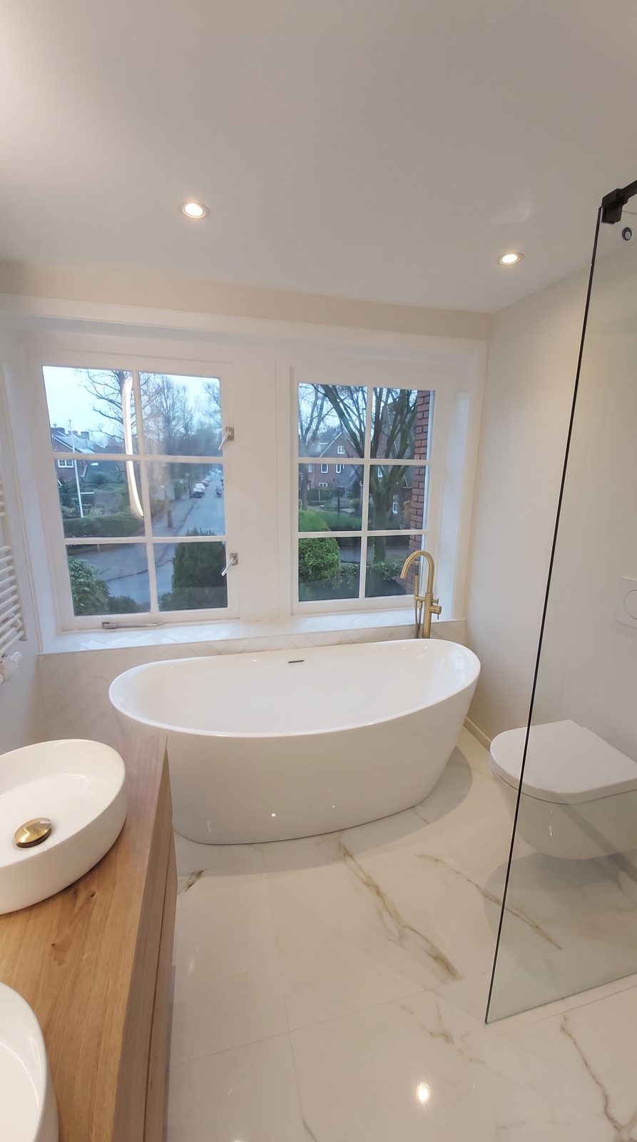 Vrijstaand bad bij het raam in een lichte badkamer met marmerlook-vloer